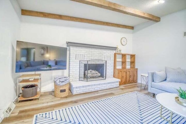 living room featuring beamed ceiling, light hardwood / wood-style flooring, and a brick fireplace