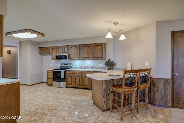 kitchen with wood walls, appliances with stainless steel finishes, decorative light fixtures, a kitchen bar, and kitchen peninsula