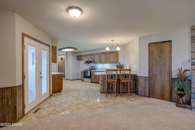 kitchen with french doors, wood walls, pendant lighting, light carpet, and appliances with stainless steel finishes