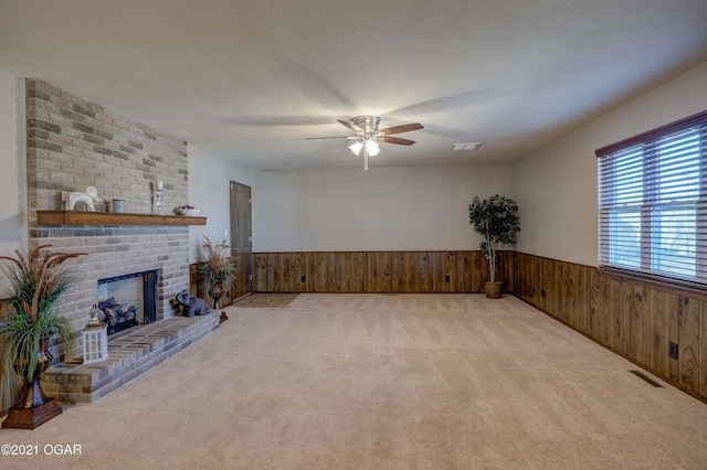 unfurnished living room featuring a textured ceiling, light colored carpet, a brick fireplace, and ceiling fan