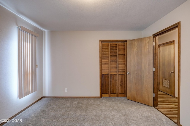 unfurnished bedroom featuring light colored carpet, a textured ceiling, and a closet