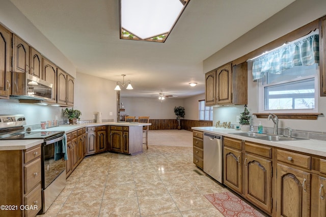 kitchen featuring pendant lighting, ceiling fan with notable chandelier, sink, appliances with stainless steel finishes, and kitchen peninsula