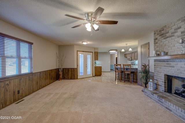 living room with light carpet, a brick fireplace, a textured ceiling, ceiling fan, and wood walls