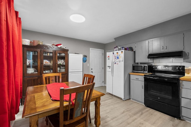 kitchen featuring white refrigerator with ice dispenser, backsplash, black electric range, gray cabinets, and light wood-type flooring