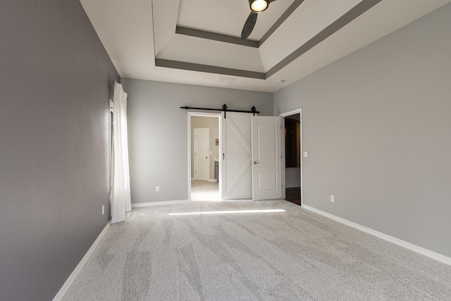 unfurnished bedroom featuring a raised ceiling, a barn door, ceiling fan, and carpet floors