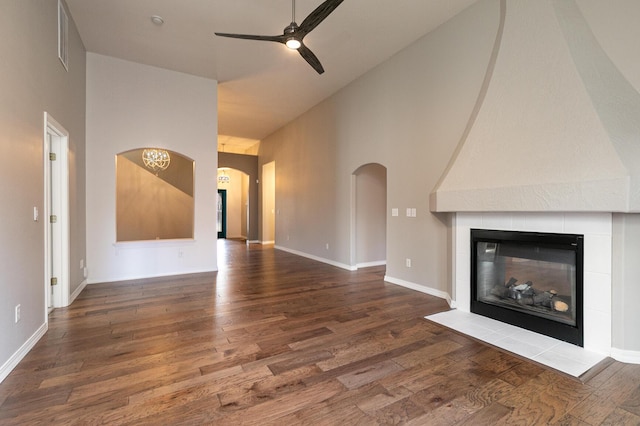 unfurnished living room with a tile fireplace, ceiling fan, dark wood-type flooring, and a high ceiling