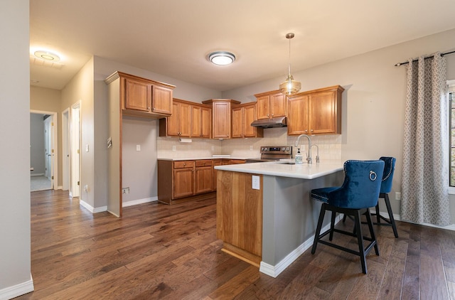 kitchen featuring electric range, sink, tasteful backsplash, kitchen peninsula, and a kitchen bar