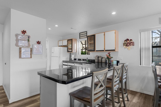 kitchen featuring a breakfast bar, white refrigerator, sink, dark hardwood / wood-style floors, and kitchen peninsula