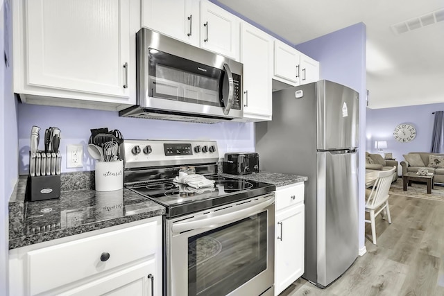 kitchen featuring light wood-type flooring, stainless steel appliances, white cabinetry, and dark stone countertops