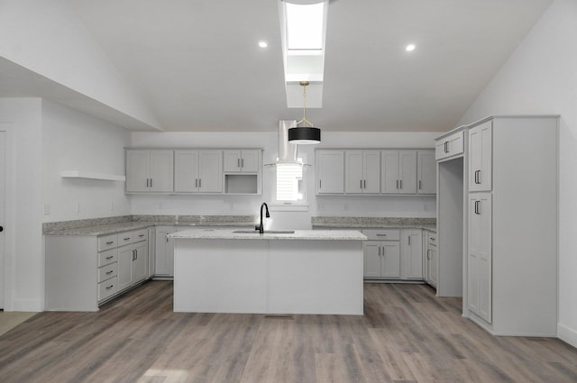 kitchen with vaulted ceiling, light stone counters, sink, and an island with sink