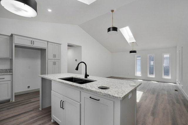 kitchen featuring a kitchen island with sink, sink, hanging light fixtures, vaulted ceiling with skylight, and light stone counters