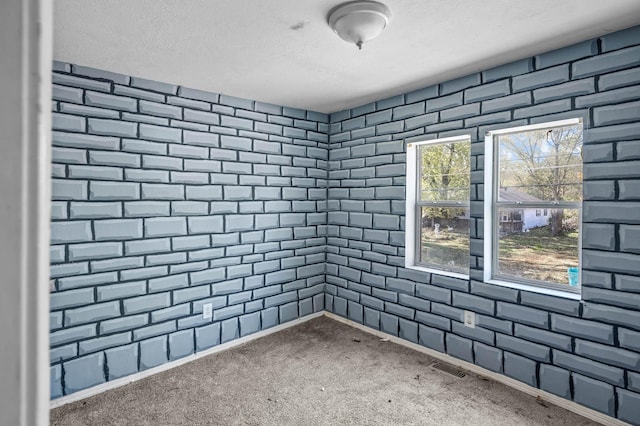 carpeted empty room with brick wall