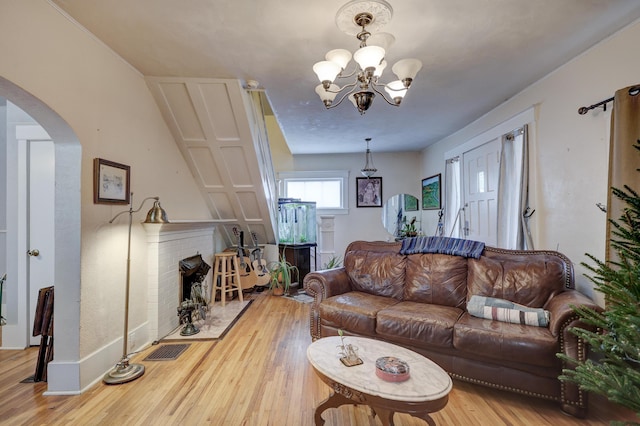 living room featuring a brick fireplace, an inviting chandelier, and light wood-type flooring