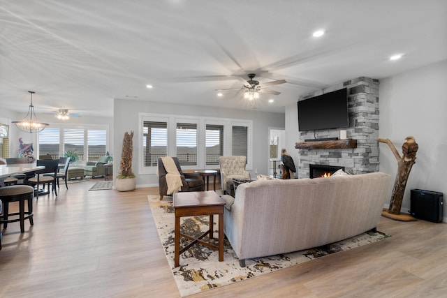 living room featuring a fireplace, light wood-type flooring, and ceiling fan with notable chandelier