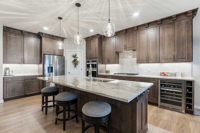 kitchen with pendant lighting, appliances with stainless steel finishes, a kitchen island with sink, and beverage cooler