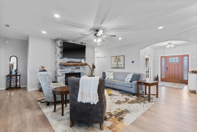 living room featuring ceiling fan, a stone fireplace, and light hardwood / wood-style flooring