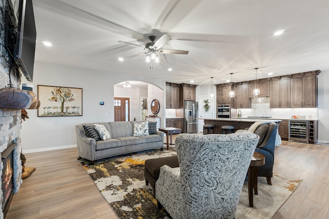 living room with a fireplace, light wood-type flooring, wine cooler, and ceiling fan