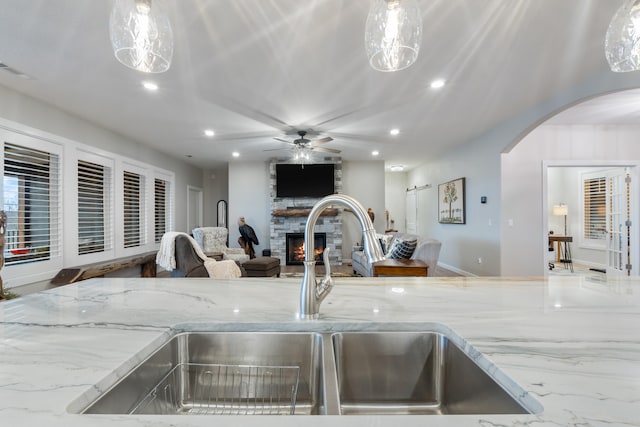 interior details featuring light stone countertops, ceiling fan, sink, decorative light fixtures, and a fireplace