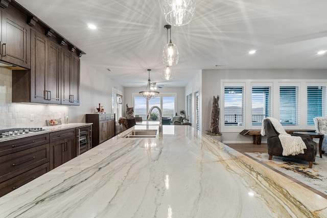 kitchen with backsplash, hanging light fixtures, wine cooler, sink, and stainless steel gas cooktop