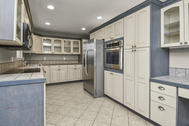 kitchen featuring tile countertops, sink, light tile patterned floors, and appliances with stainless steel finishes