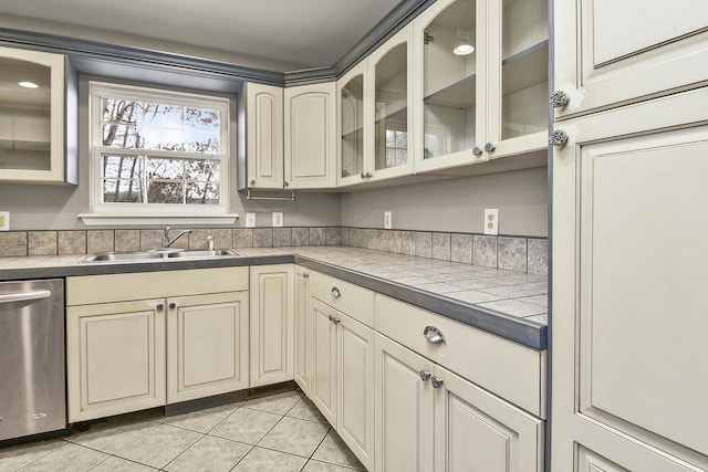 kitchen featuring tile counters, sink, stainless steel dishwasher, cream cabinets, and light tile patterned floors