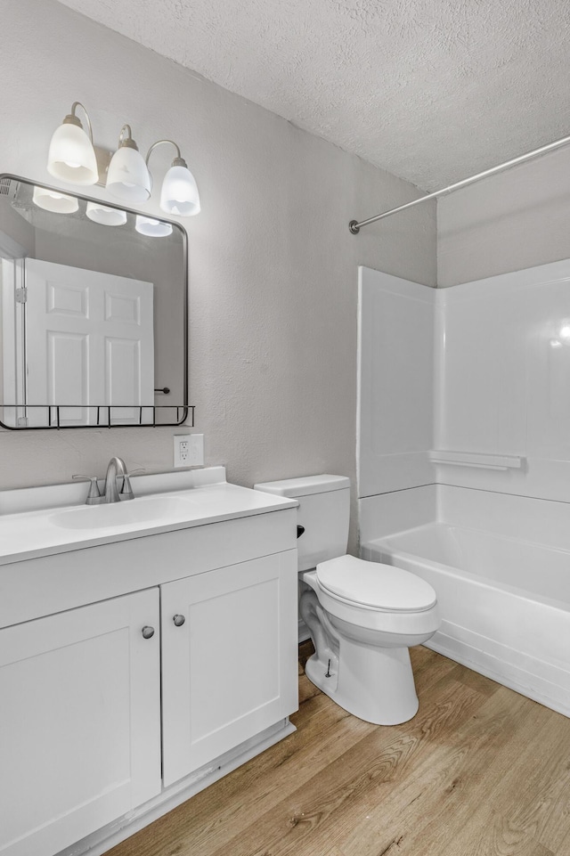 full bathroom with vanity, a textured ceiling,  shower combination, hardwood / wood-style floors, and toilet