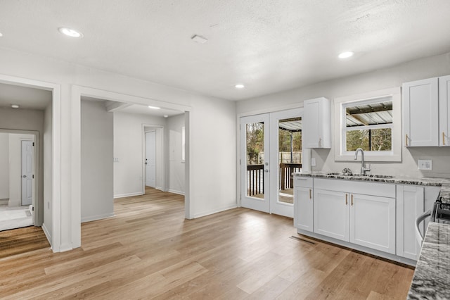 kitchen with white cabinetry, sink, a textured ceiling, stone countertops, and light wood-type flooring