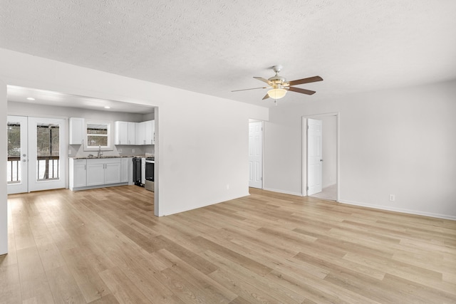 unfurnished living room featuring french doors, sink, ceiling fan, light wood-type flooring, and a textured ceiling