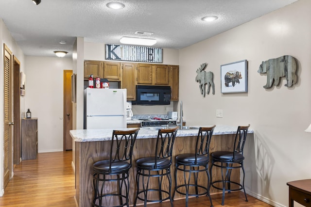 kitchen with a kitchen breakfast bar, white refrigerator, kitchen peninsula, light hardwood / wood-style floors, and a textured ceiling