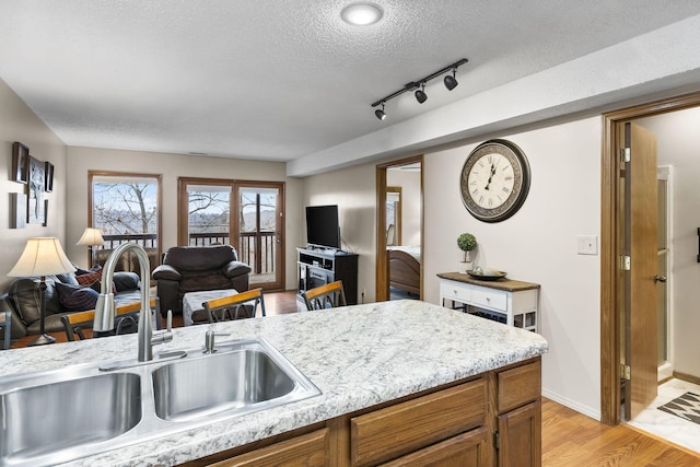 kitchen with track lighting, light stone counters, a textured ceiling, sink, and light hardwood / wood-style floors