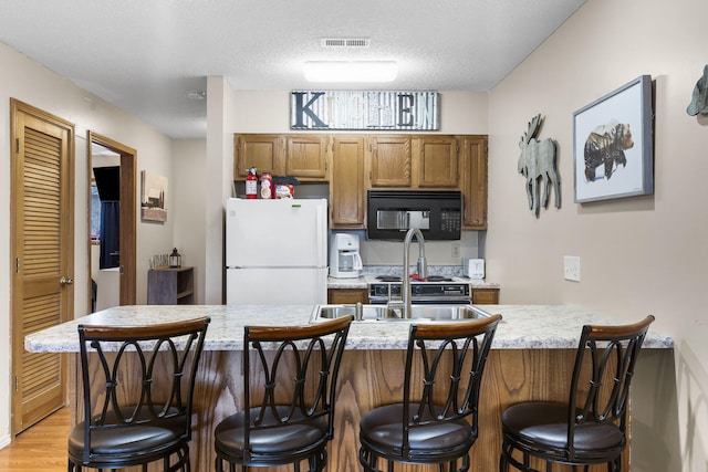 kitchen featuring a kitchen breakfast bar, white fridge, a textured ceiling, and light wood-type flooring