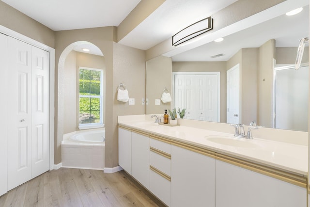 bathroom with hardwood / wood-style floors, vanity, and tiled bath