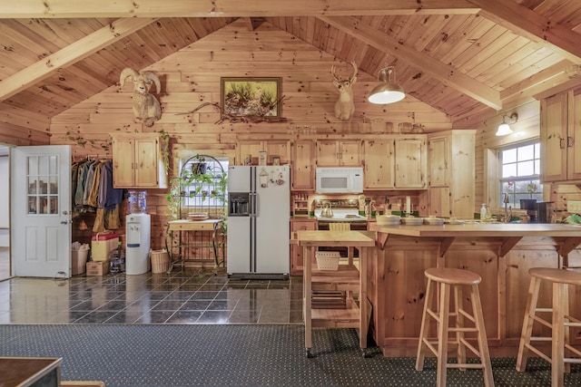 kitchen featuring beamed ceiling, light brown cabinetry, white appliances, and wood walls