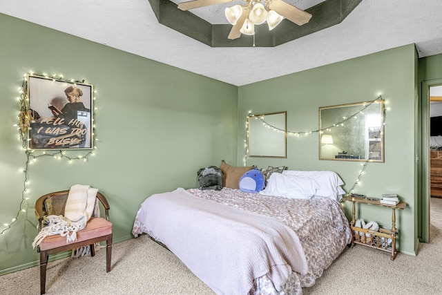 bedroom with ceiling fan, carpet floors, a textured ceiling, and a tray ceiling