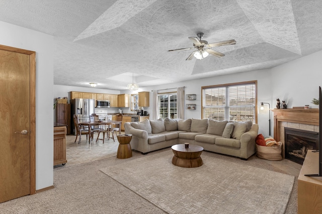 tiled living room with a tray ceiling, a tiled fireplace, and ceiling fan