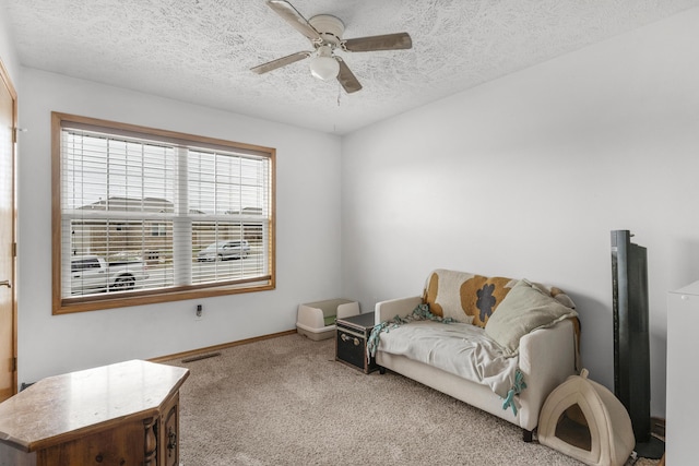 sitting room with ceiling fan, light colored carpet, and a textured ceiling