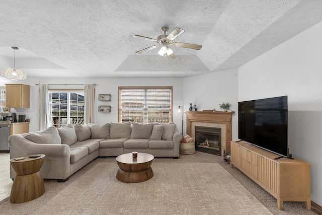 living room featuring ceiling fan, light colored carpet, a tile fireplace, and a tray ceiling