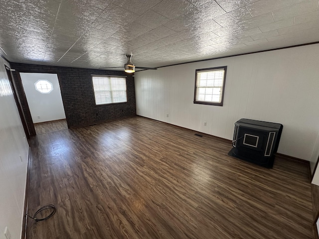 empty room featuring a wood stove, ceiling fan, dark wood-type flooring, and brick wall