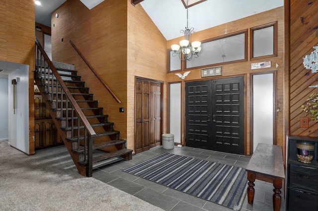 carpeted entrance foyer featuring high vaulted ceiling, beam ceiling, wooden walls, and an inviting chandelier