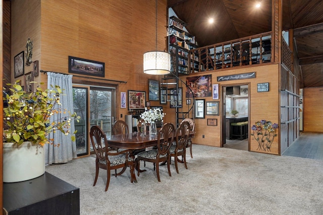 carpeted dining area with high vaulted ceiling, wooden walls, and wooden ceiling