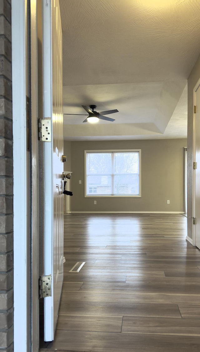 empty room with a raised ceiling, ceiling fan, and dark wood-type flooring