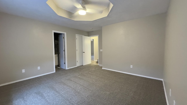 unfurnished bedroom featuring ceiling fan, dark carpet, and a tray ceiling