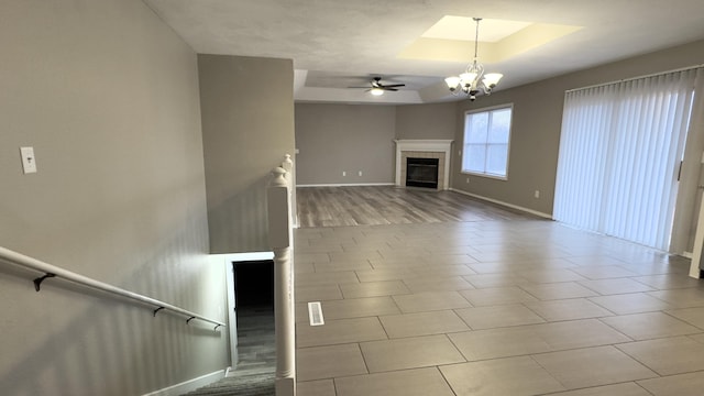 unfurnished living room with a tray ceiling, a fireplace, and ceiling fan with notable chandelier