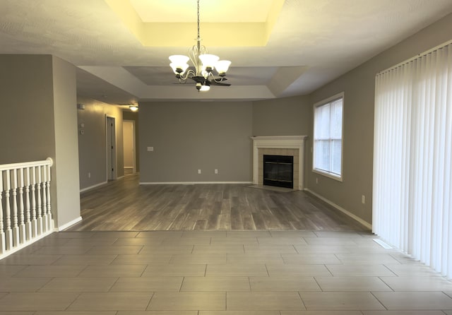 unfurnished living room featuring a tray ceiling, an inviting chandelier, and a tiled fireplace