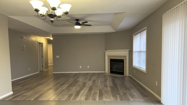 unfurnished living room with a raised ceiling, a fireplace, dark wood-type flooring, and ceiling fan with notable chandelier