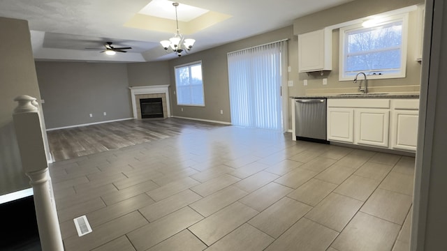 kitchen featuring white cabinetry, sink, stainless steel dishwasher, pendant lighting, and a tray ceiling