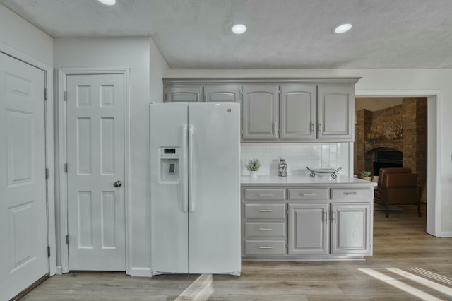 kitchen featuring gray cabinetry, white fridge with ice dispenser, tasteful backsplash, light hardwood / wood-style flooring, and a textured ceiling