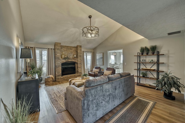 living room featuring a notable chandelier, plenty of natural light, light wood-type flooring, and a brick fireplace