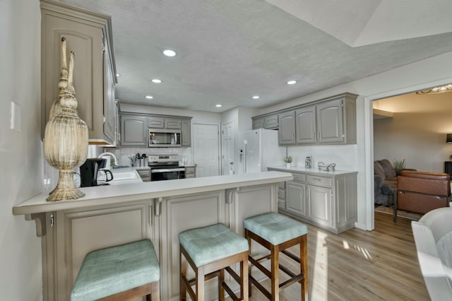 kitchen featuring a breakfast bar area, gray cabinetry, kitchen peninsula, and appliances with stainless steel finishes