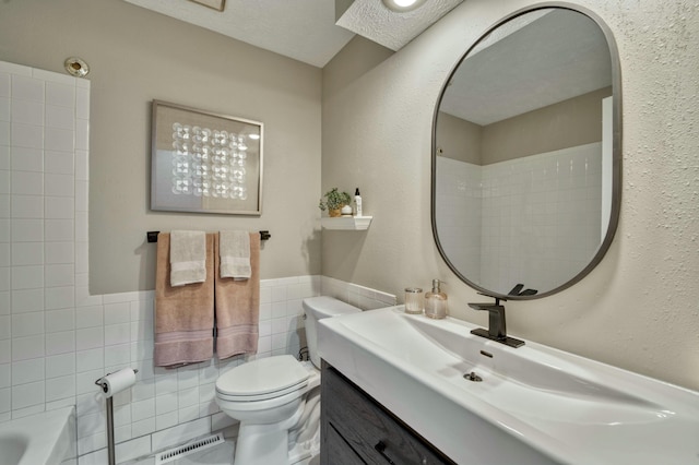 full bathroom featuring tiled shower / bath combo, a textured ceiling, toilet, vanity, and tile walls